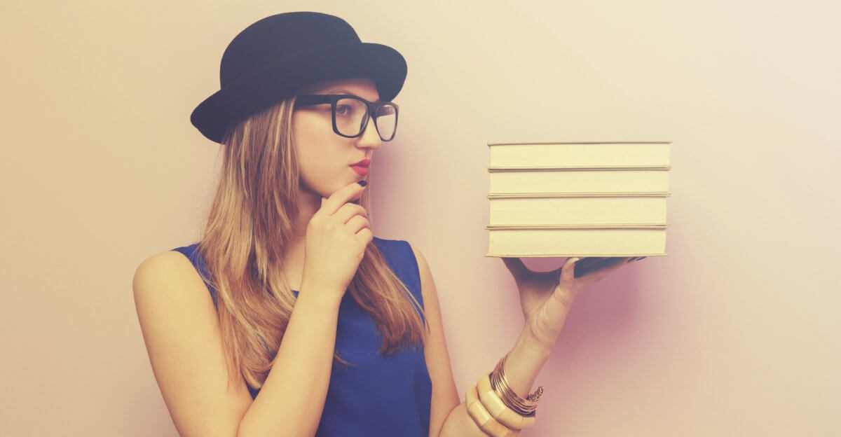 Eine Studentin hält einen Stapel Bücher hoch und legt Daumen und Zeigefinger in einer Denkerpose an ihr Kinn.