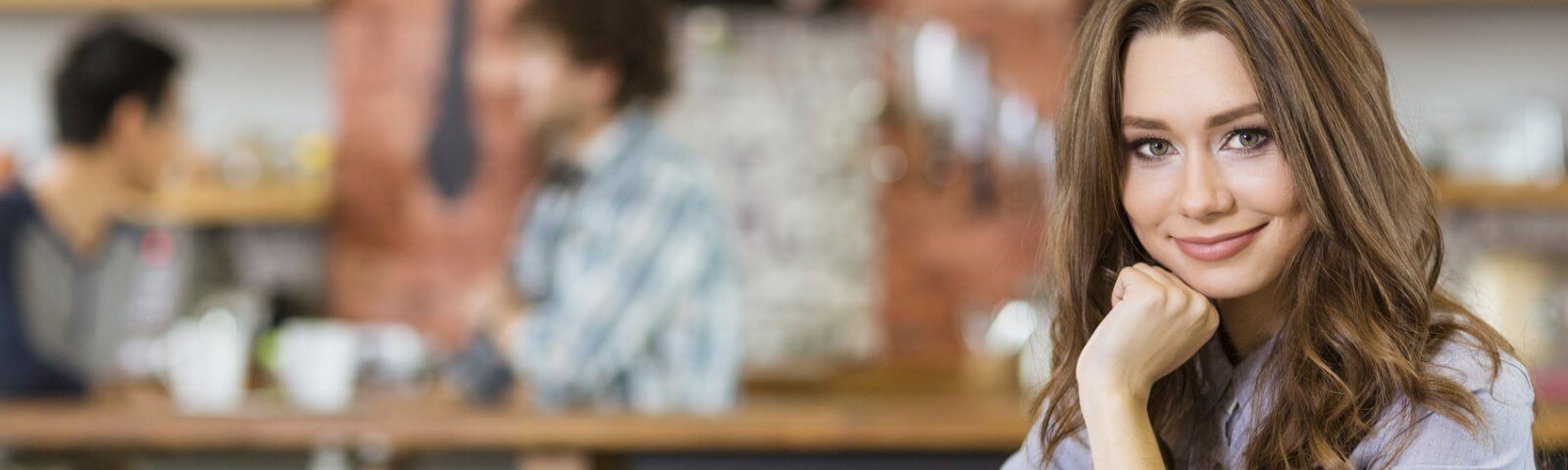 Eine Studentin sitzt am Tisch in einem Café und stützt ihr Kinn mit der Hand ab.