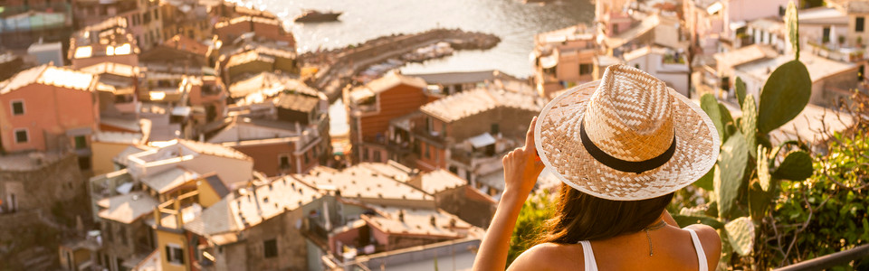 Rückansicht einer Frau mit Sonnenhut, die auf Hafenstadt und Wasser hinunterschaut