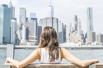 Eine Studentin sitzt auf einer Bank und betrachtet die Skyline von New York.