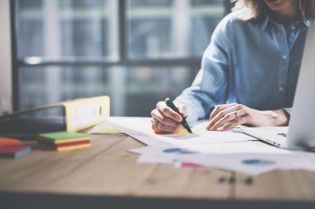 Eine Studentin markiert mit Textmarker etwas auf einem Blatt Papier, auf dem Tisch verteilt liegen Arbeitsmaterialien.