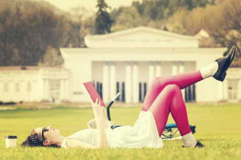 Eine Studentin liegt auf dem Rasen und liest in einem Buch.