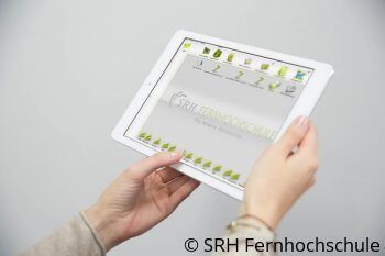 Hände halten ein Tablet, auf dem die Online-Lernplattform der SRH Fernhochschule geöffnet ist